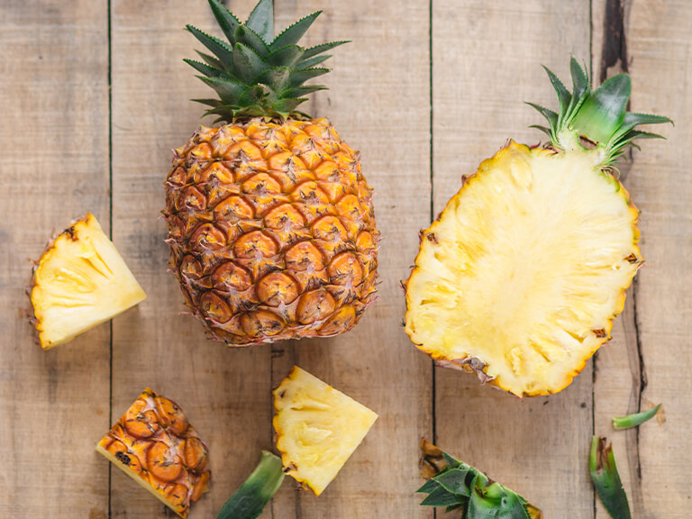 Photo of pineapples with one cut half as well as slices