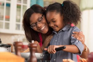 Mom hugging daughter while daughter is cooking on stovetop